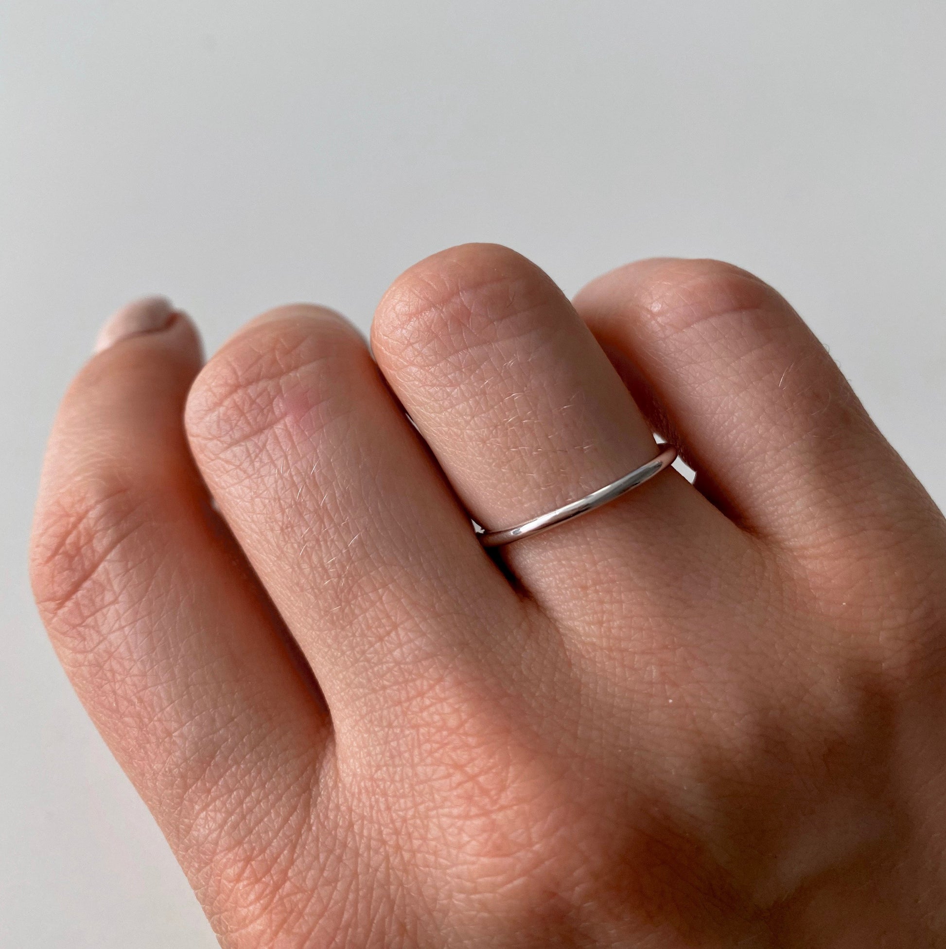 Ръка с обикновен сребърен пръстен на светъл фон.