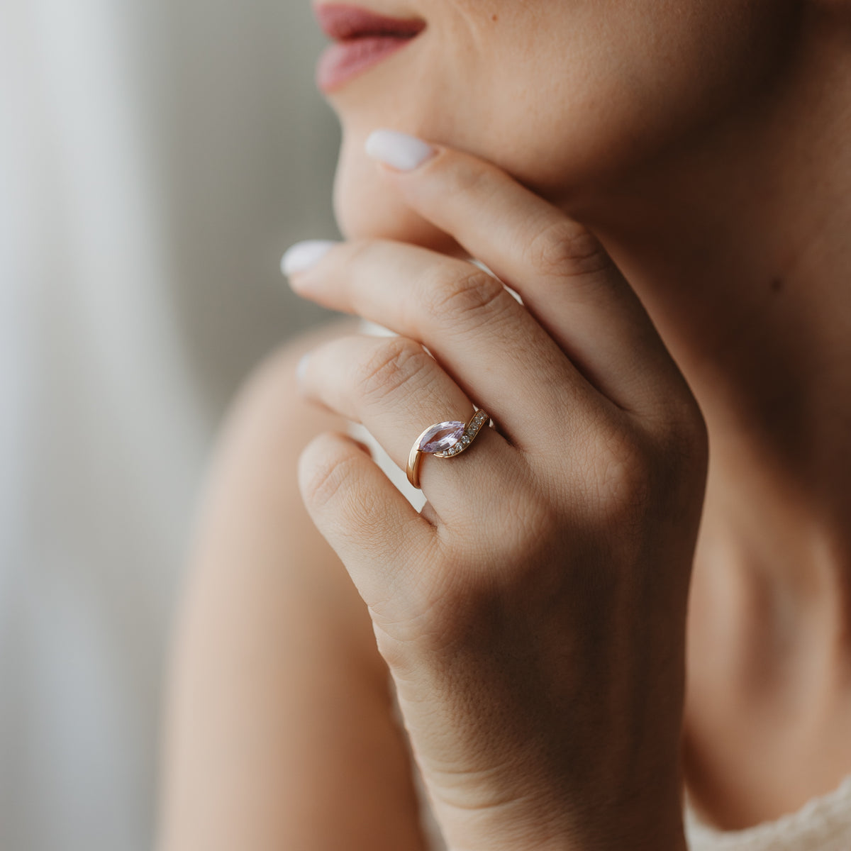 Близък план на ръка до лицето с пръстен Velvet Rose от 14K жълто злато, украсен с розов сапфир с шлифовка маркиз и малки акцентни диаманти.